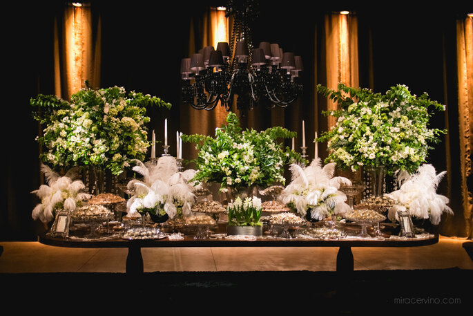 Mesa de doces com arranjos brancos e verdes, plumas e candelabros, no casamento de Rogério e Gustavo